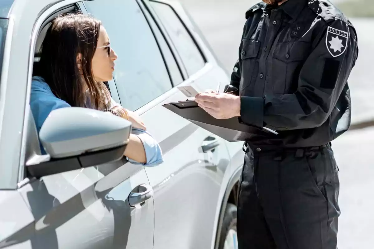 Una mujer en un coche hablando con un oficial de policía que sostiene una libreta y un bolígrafo.