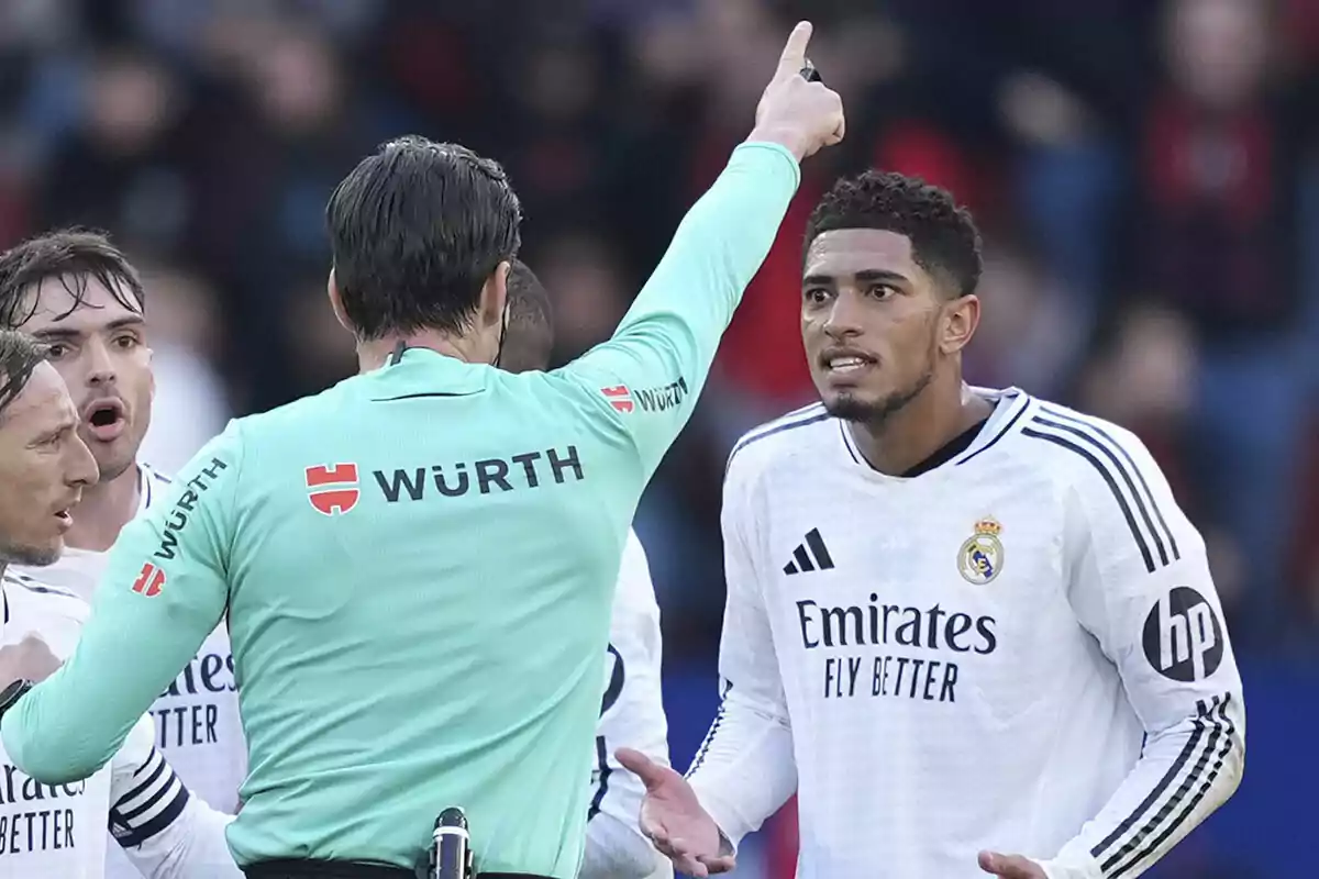 Un árbitro señala con el dedo mientras un jugador del Real Madrid reacciona durante un partido de fútbol.