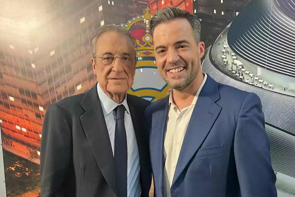 Florentino Pérez y Nacho Peña con trajes posando juntos frente a un fondo de edificios iluminados y un escudo del Real Madrid.