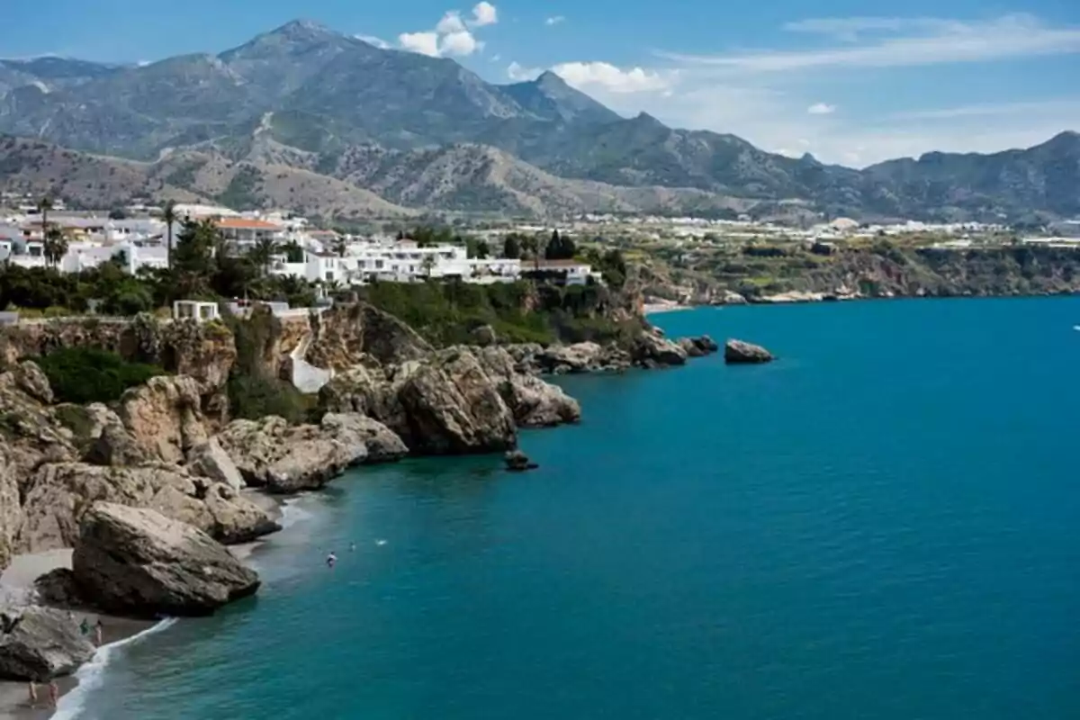 Vista panorámica de una costa rocosa con casas blancas y montañas al fondo.