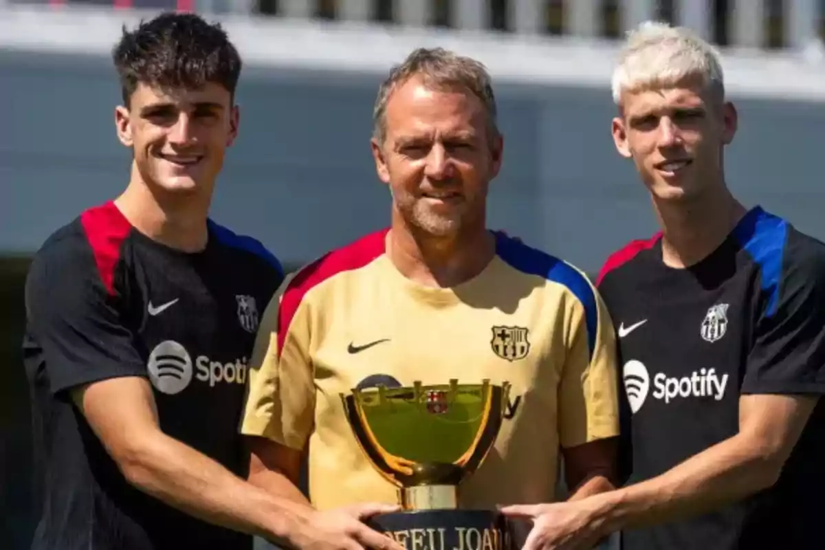 Three people pose with a FC Barcelona trophy at a training ground.