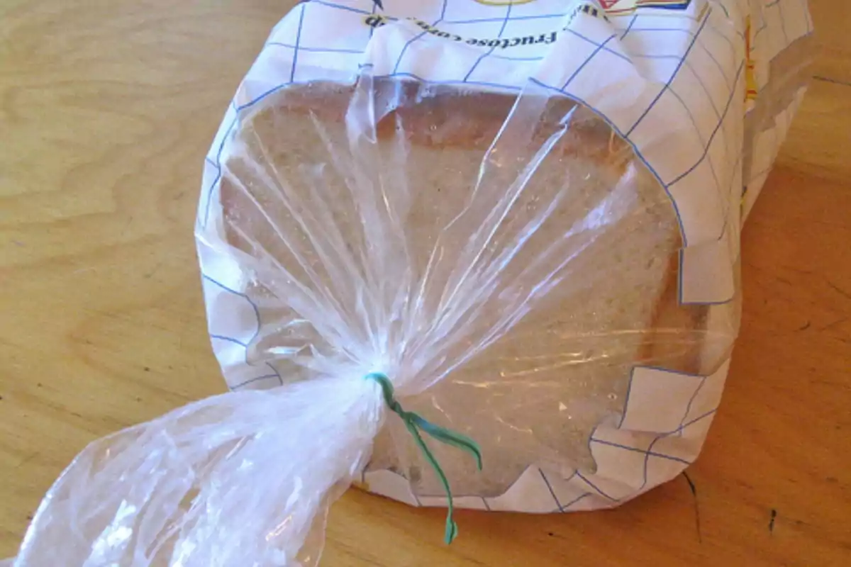 Un paquete de pan de molde envuelto en una bolsa de plástico transparente y cerrado con un alambre verde sobre una mesa de madera.