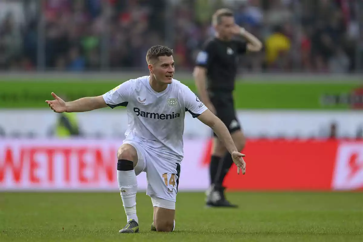 Bayer Leverkusen player kneeling on the field with arms outstretched during a match