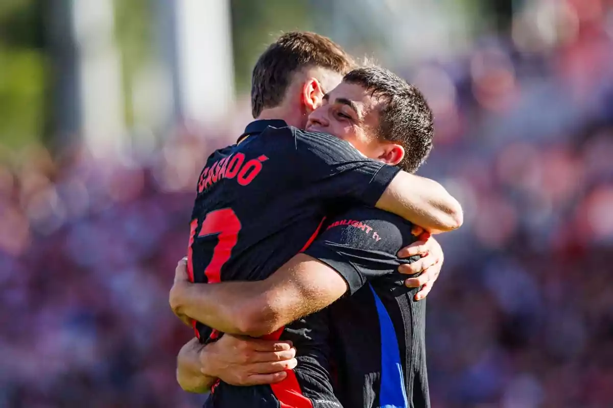 Dos jugadores de fútbol se abrazan celebrando un gol en un partido.