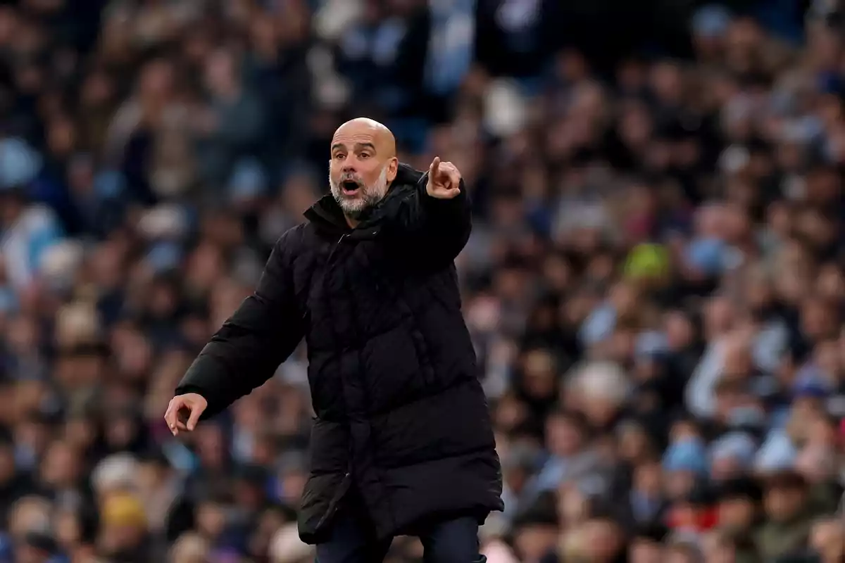 A man in a black coat gestures in a stadium full of spectators.