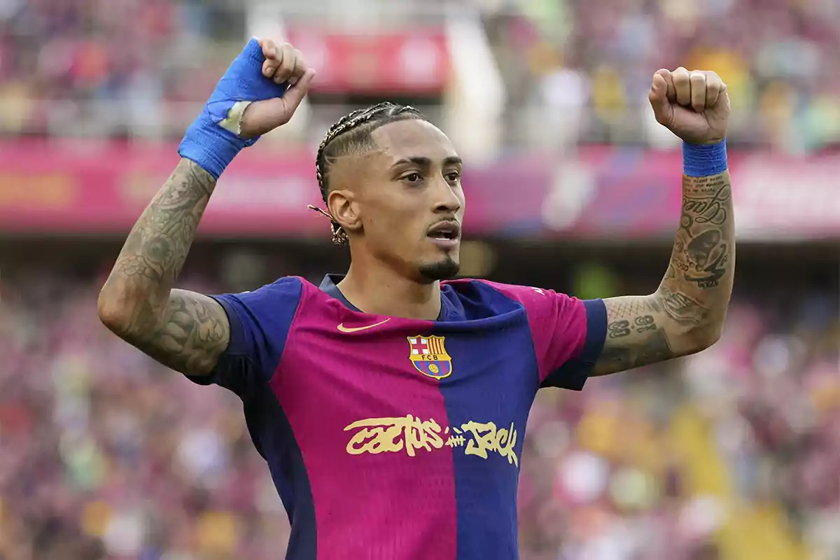 Jugador de fútbol con uniforme azul y rosa levantando los brazos en señal de celebración en un estadio. Jugador de fútbol con uniforme azul y rosa levantando los brazos en señal de celebración en un estadio.