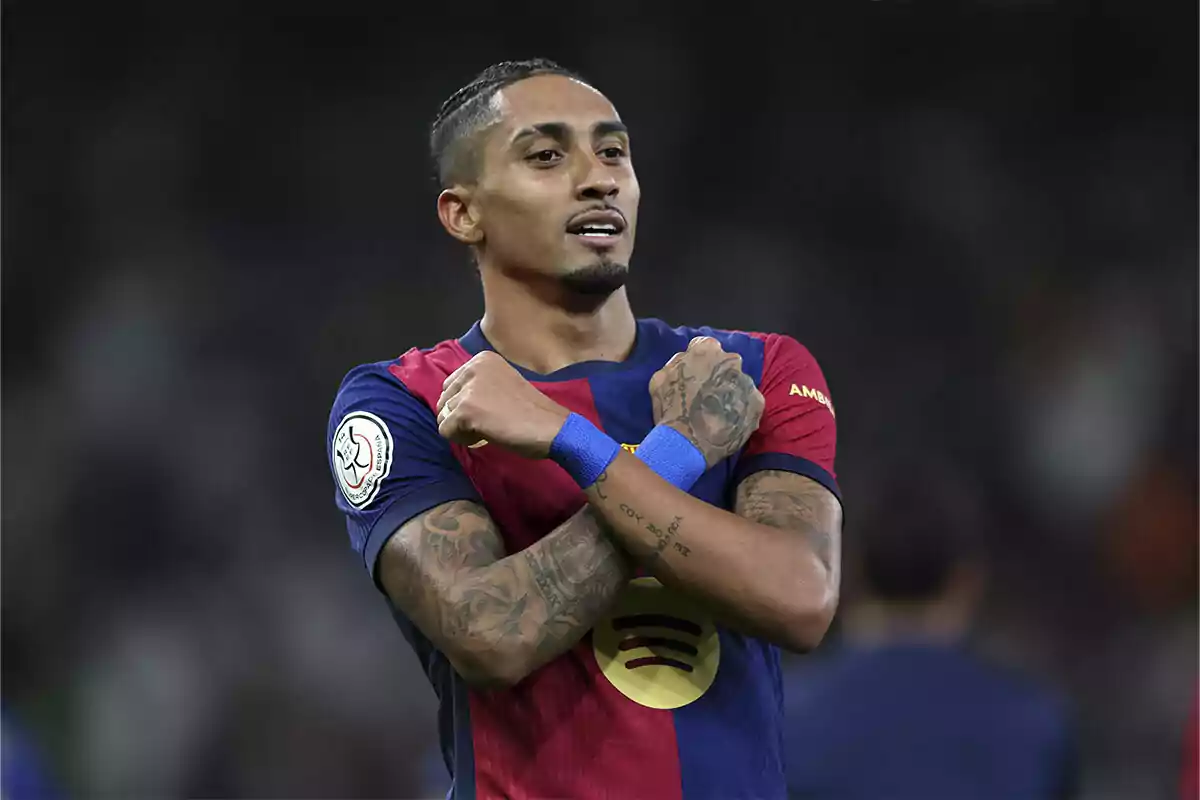 A soccer player in a blue and red uniform celebrates with his arms crossed over his chest.