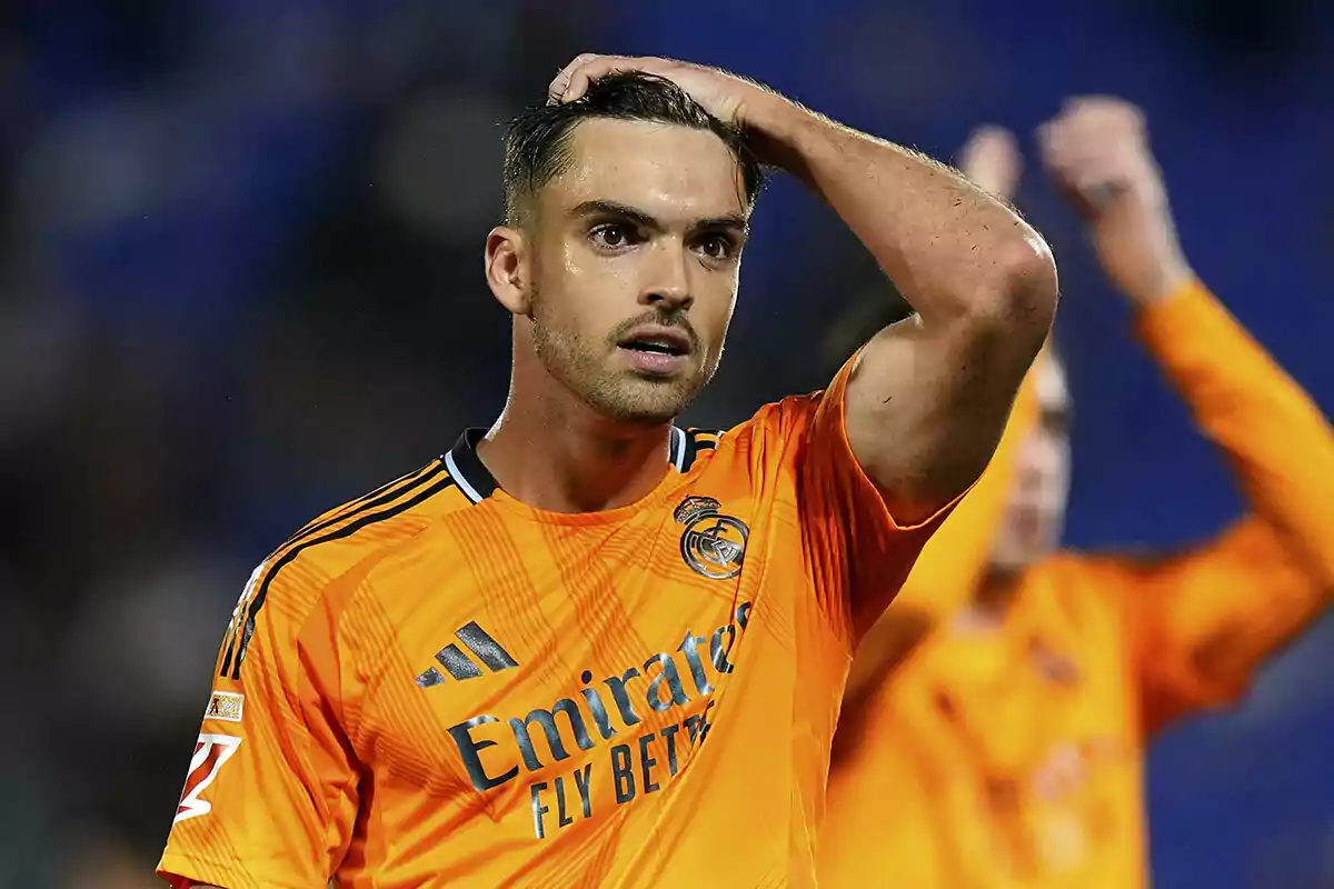 Raúl Asencio con uniforme naranja del Real Madrid en el campo con expresión de sorpresa. Raúl Asencio con uniforme naranja del Real Madrid en el campo con expresión de sorpresa.