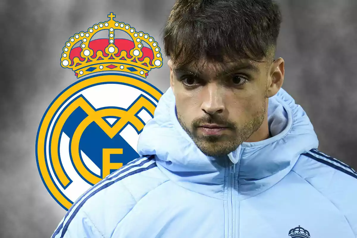 Raúl Asencio con una chaqueta azul claro frente al escudo del Real Madrid.