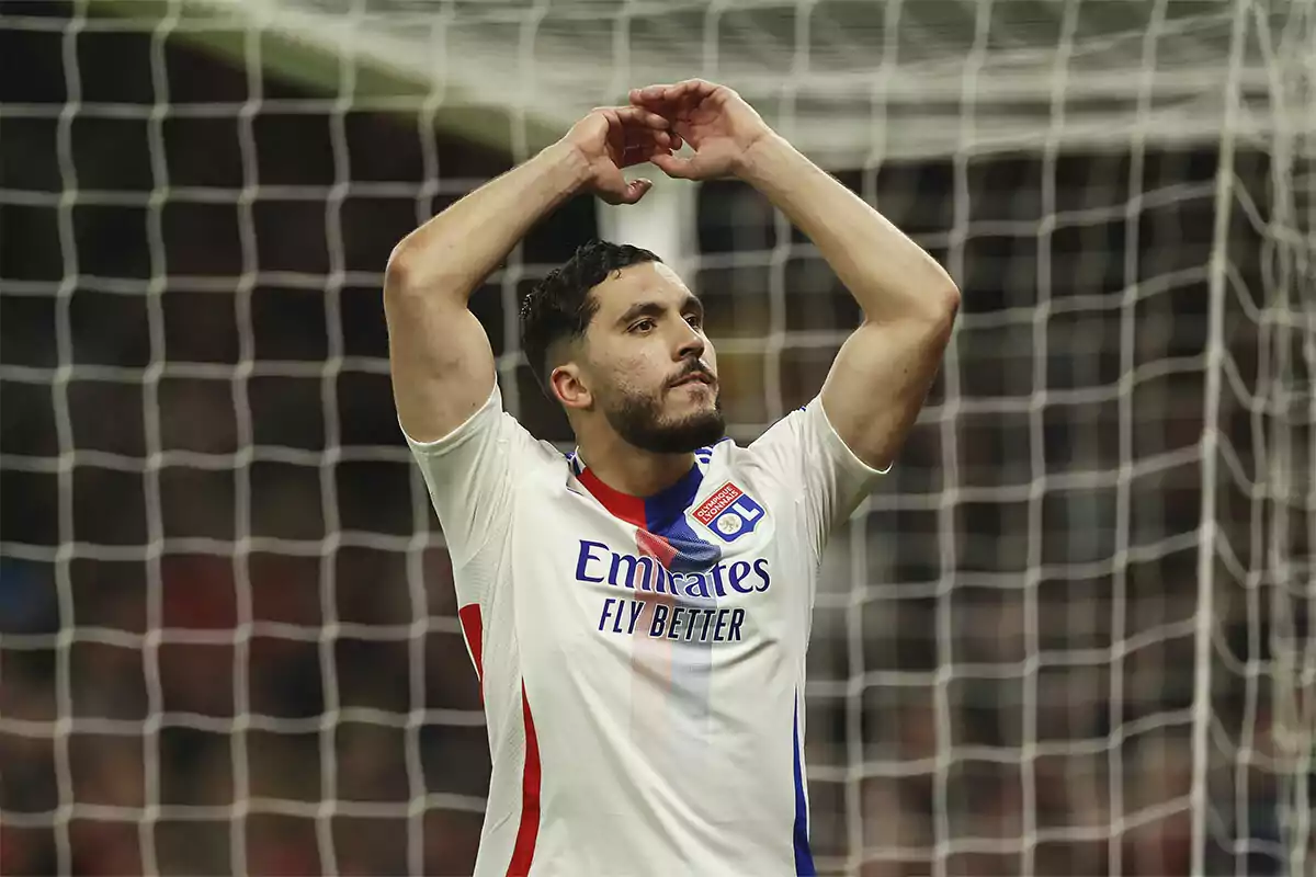A player in a white and blue uniform is standing in front of a goal with his arms raised above his head. A player in a white and blue uniform is standing in front of a goal with his arms raised above his head.