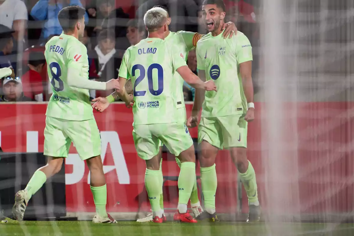 Football players celebrating a goal on the field in green uniforms.