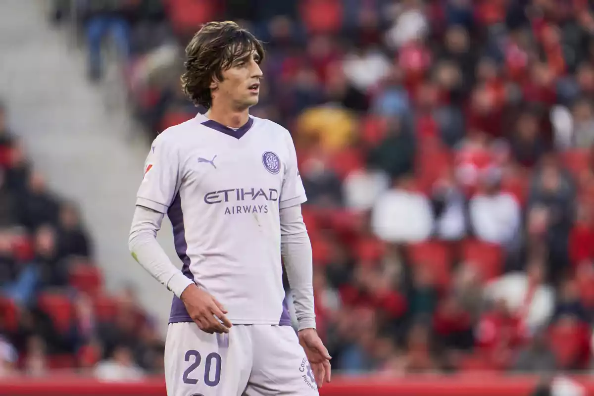 Soccer player in white uniform with purple details in a stadium with an audience in the background. Soccer player in white uniform with purple details in a stadium with an audience in the background.
