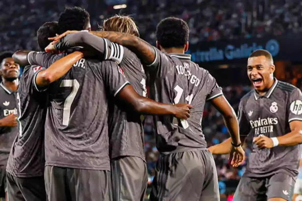 soccer players celebrating a team goal in grey uniforms in a stadium full of spectators.