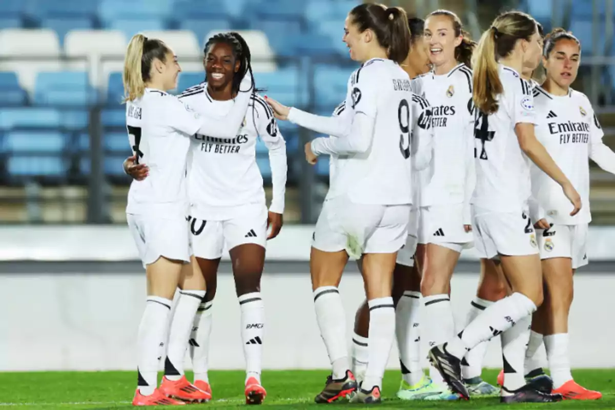 Real Madrid female players celebrating on the field in white uniforms.