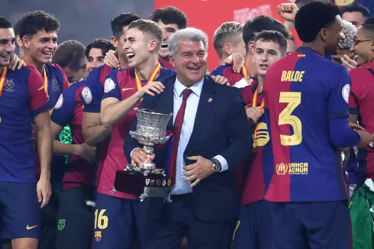 A group of soccer players celebrate with a trophy, everyone is smiling and wearing medals.