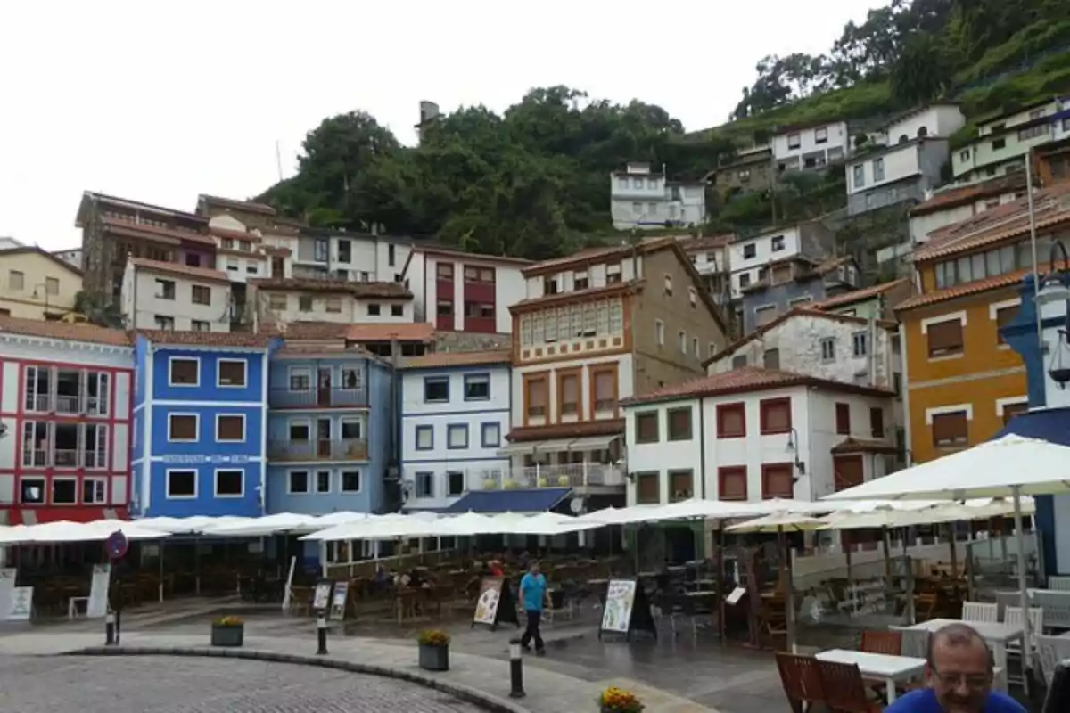 Casas coloridas en una ladera con terrazas y mesas al aire libre en la parte inferior.