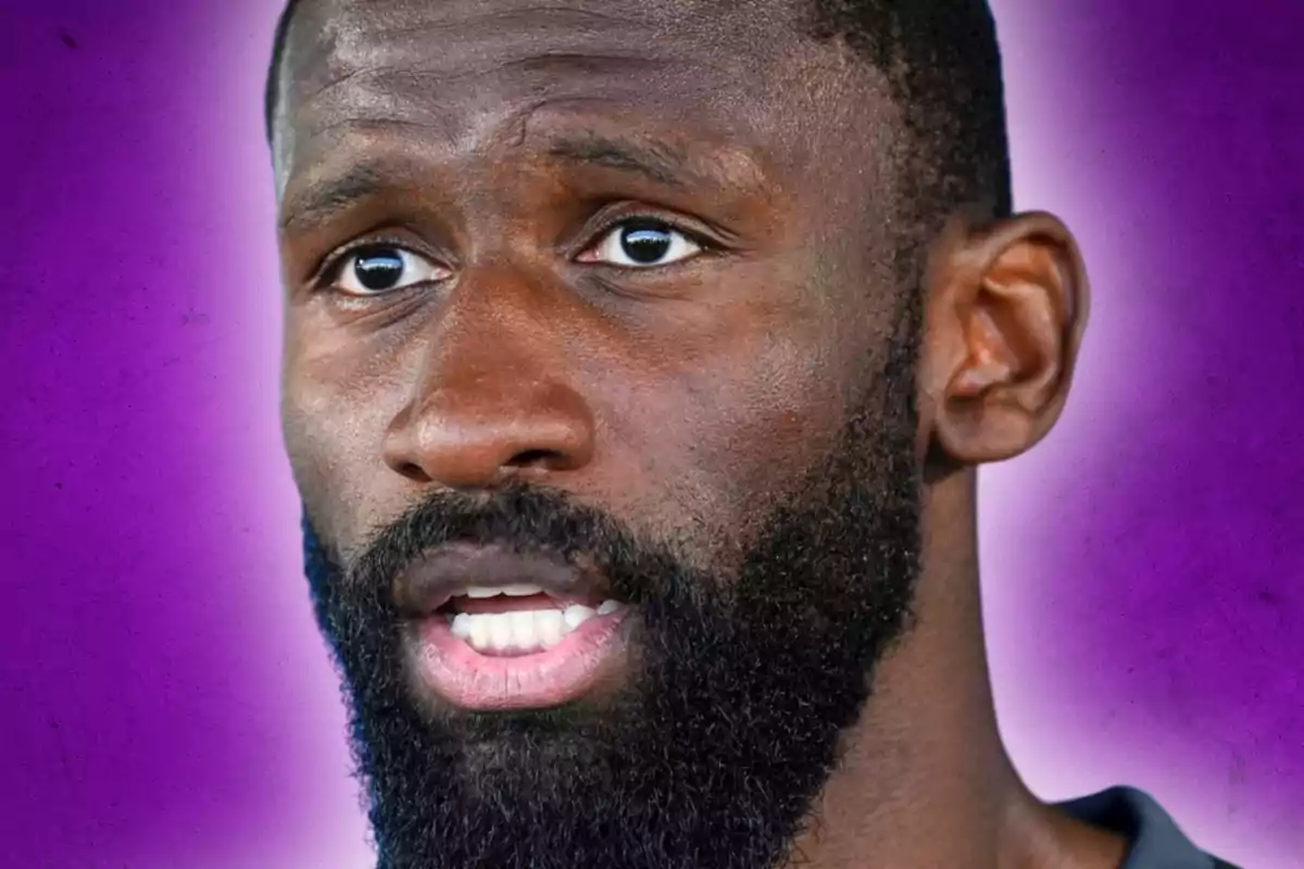 Close-up of a bearded man with a serious expression, with a blurred purple background.