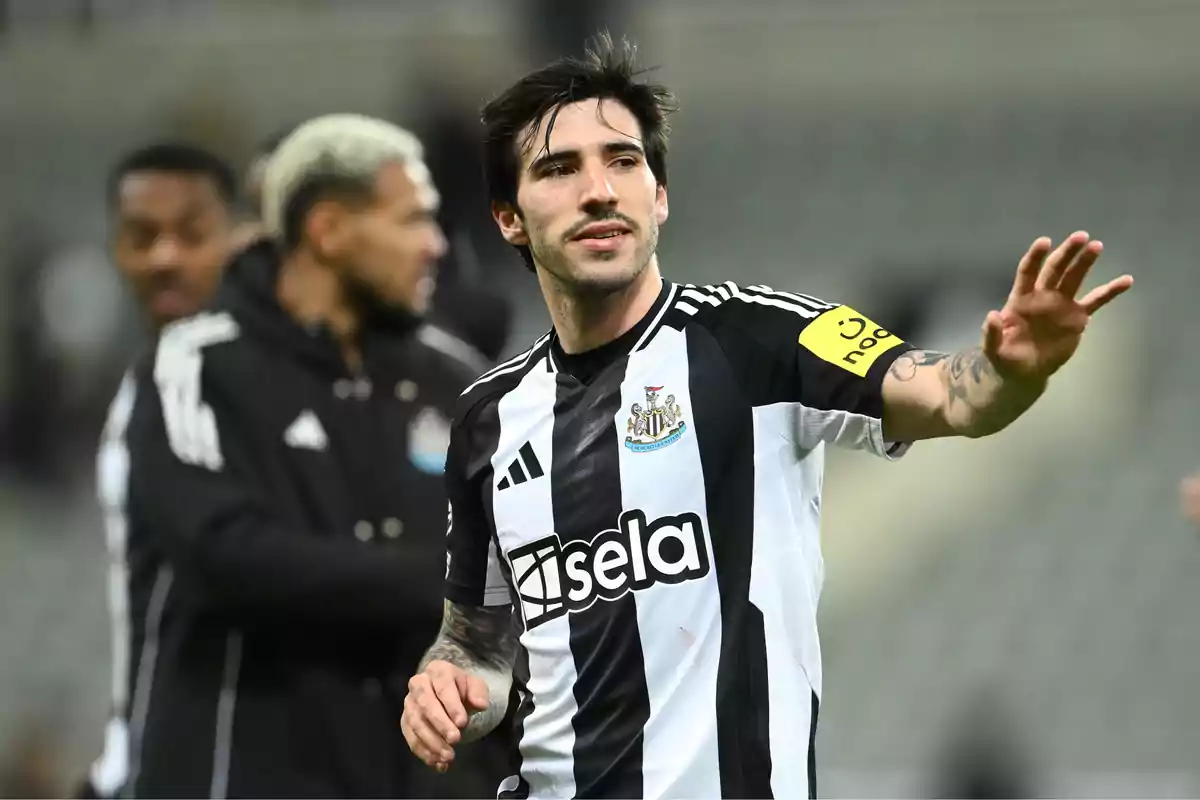 A player in a black and white uniform raises his hand on the field while other players are in the background. A player in a black and white uniform raises his hand on the field while other players are in the background.