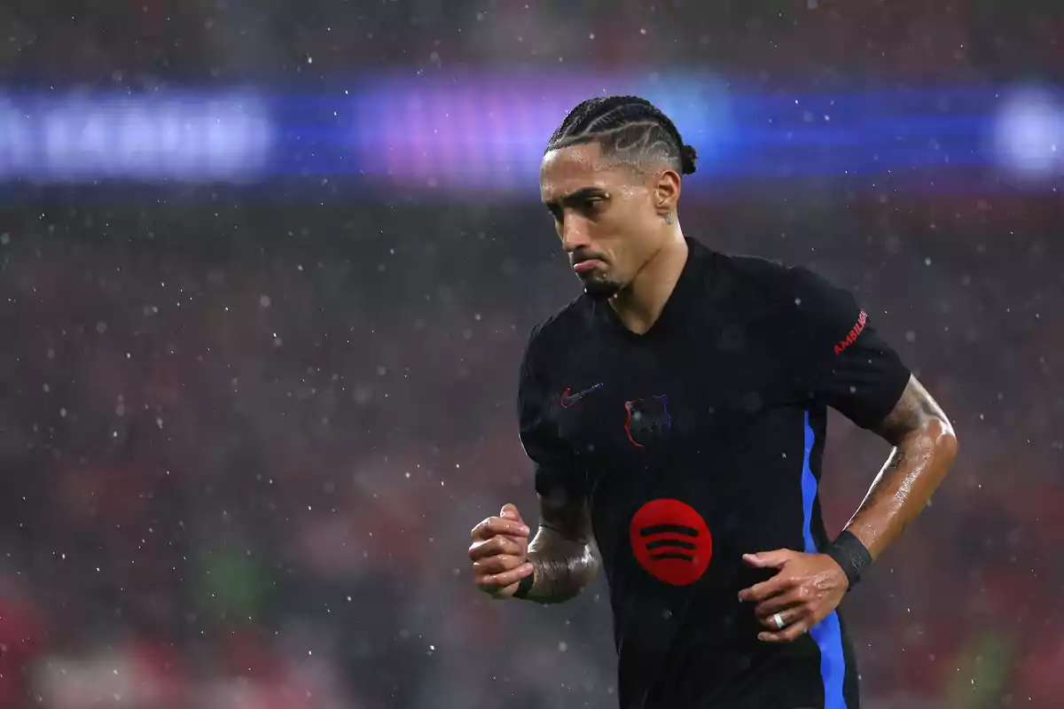 Football player wearing a black FC Barcelona jersey in the rain during a match.