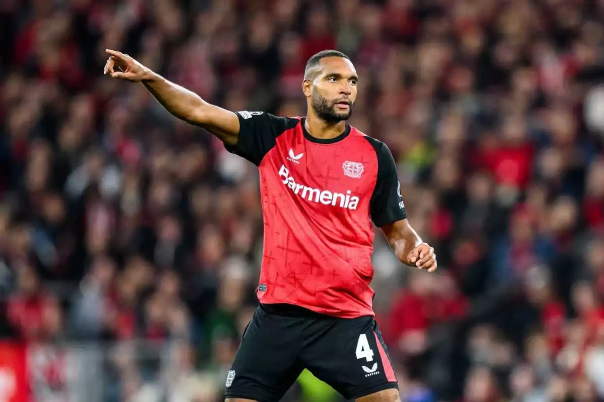 Un jugador de fútbol con uniforme rojo y negro señala hacia un lado en un estadio lleno de espectadores. Un jugador de fútbol con uniforme rojo y negro señala hacia un lado en un estadio lleno de espectadores.