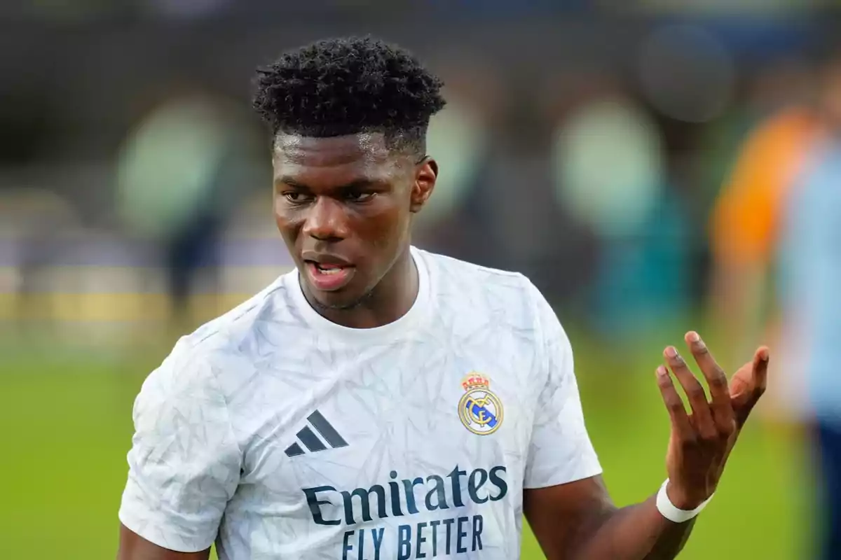 Jugador de fútbol con camiseta blanca del Real Madrid gesticulando en el campo.