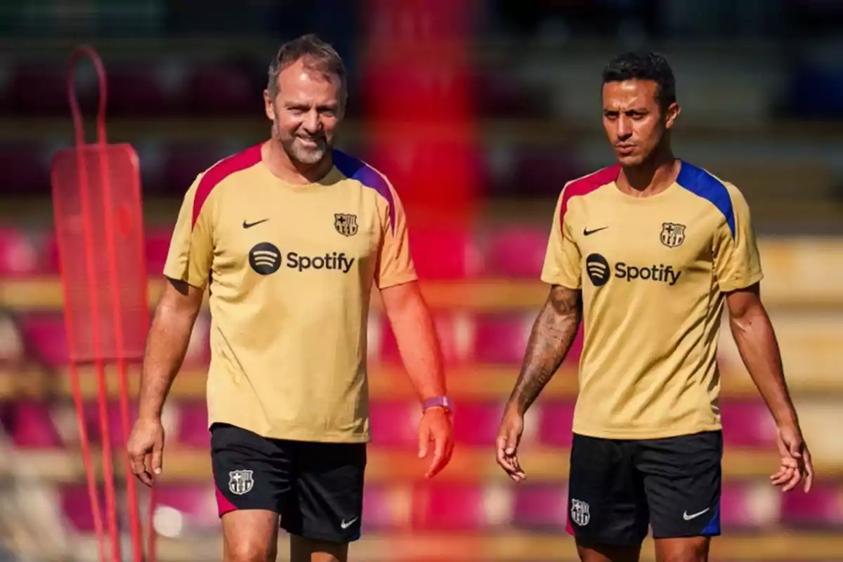 Two people wearing FC Barcelona training jerseys walking on a soccer field.