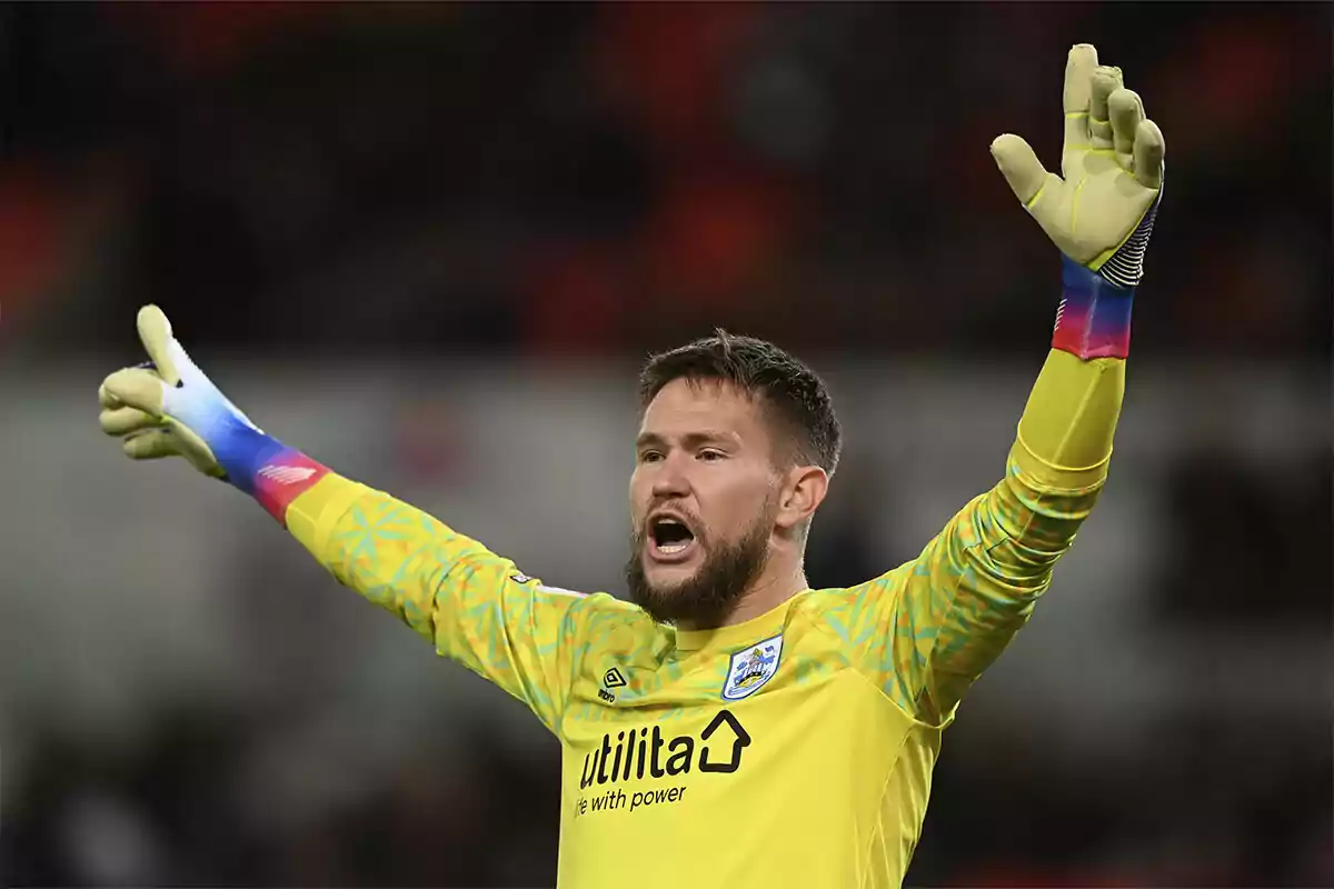 A soccer goalkeeper in a yellow uniform and gloves raises his arms on the field. A soccer goalkeeper in a yellow uniform and gloves raises his arms on the field.