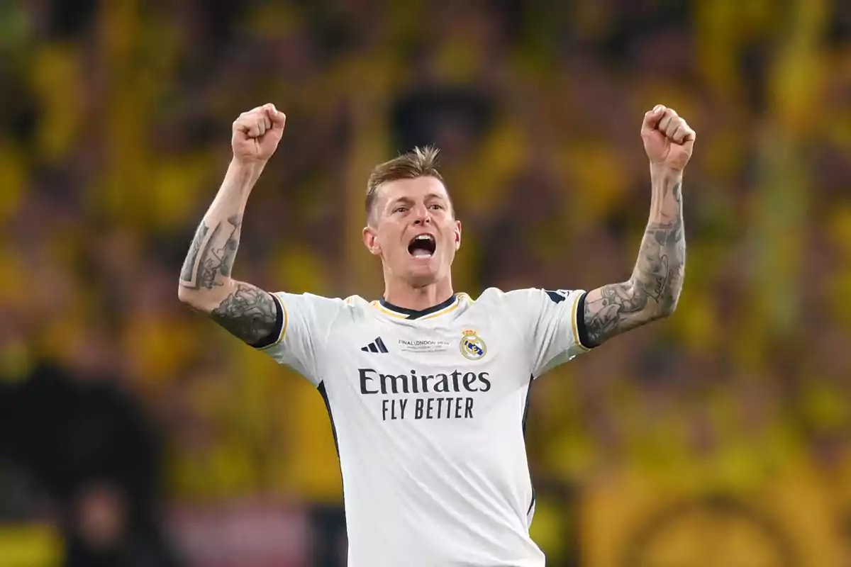 A player in a white uniform celebrates with arms raised in a stadium full of spectators.