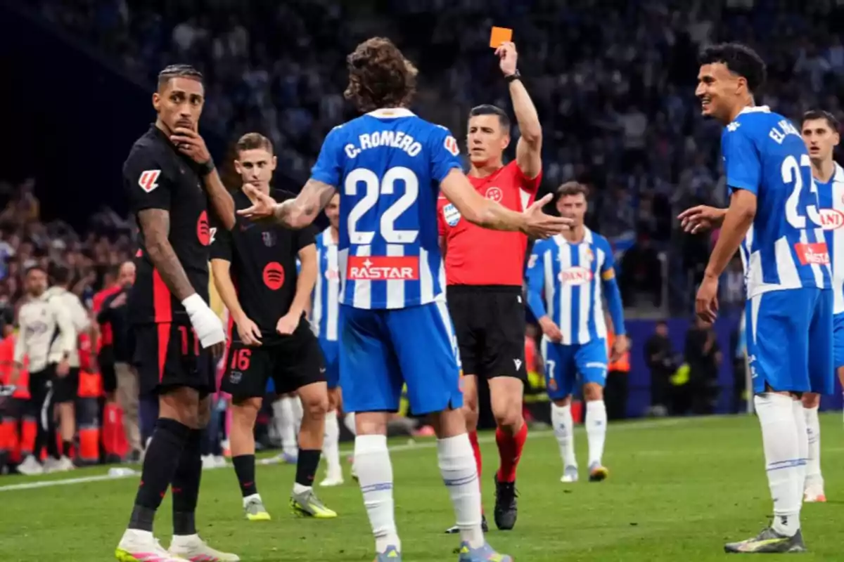 A referee shows a red card to a player in a soccer match while other players watch the situation. A referee shows a red card to a player in a soccer match while other players watch the situation.