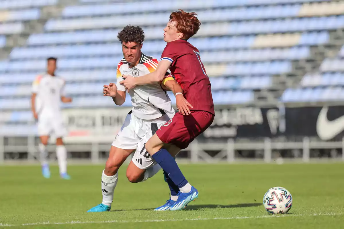 Two soccer players compete for the ball in a match in a stadium with empty stands.