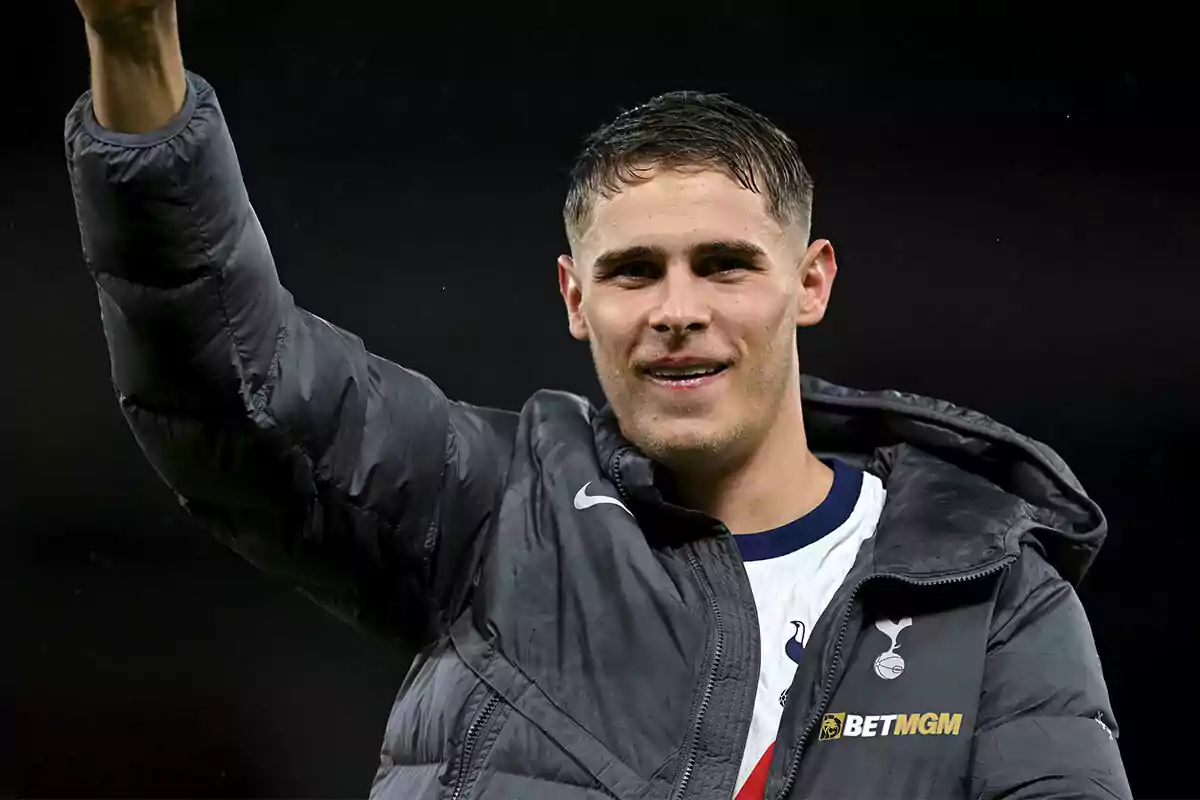 Micky van de Ven in a grey sports jacket raises his arm and smiles. Micky van de Ven in a grey sports jacket raises his arm and smiles.