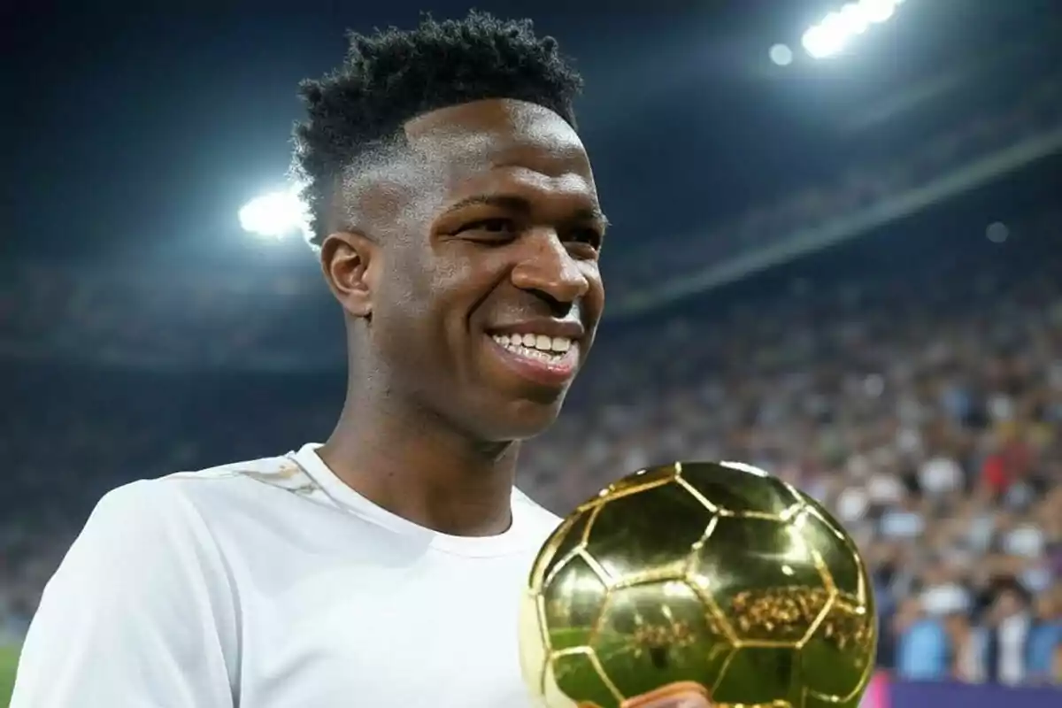 Vinícius Júnior sonríe mientras sostiene el Balón de Oro en un estadio iluminado.