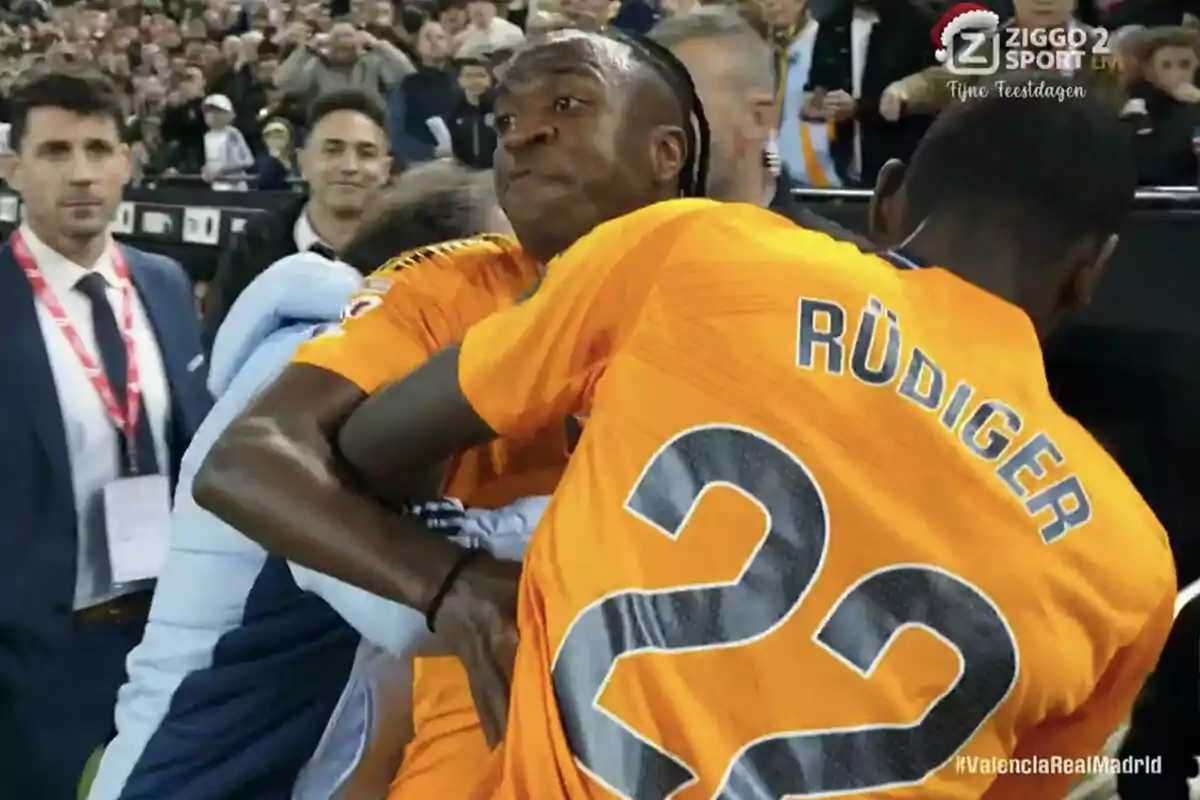 Football players in orange jerseys in a tense situation during a match, surrounded by spectators in the stands. Football players in orange jerseys in a tense situation during a match, surrounded by spectators in the stands.