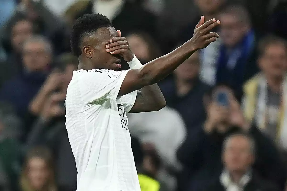 Vinícius Júnior celebrating a goal with his hand on his face in a stadium full of spectators.