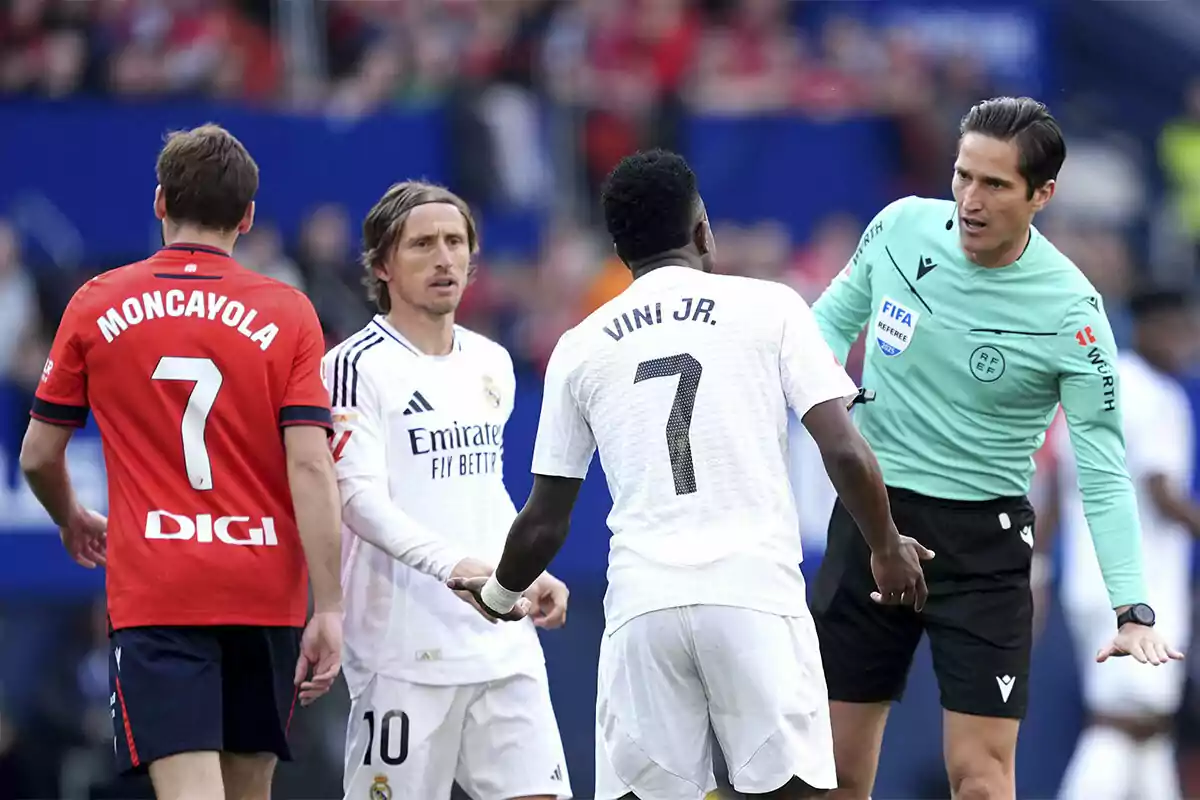 Un árbitro dialoga con jugadores de dos equipos de fútbol en el campo durante un partido.