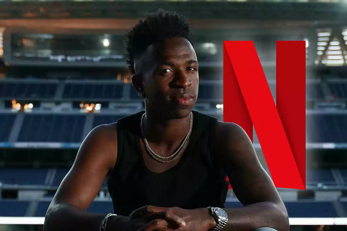A man in a black T-jersey and chains is sitting in front of a large Netflix logo in a stadium.
