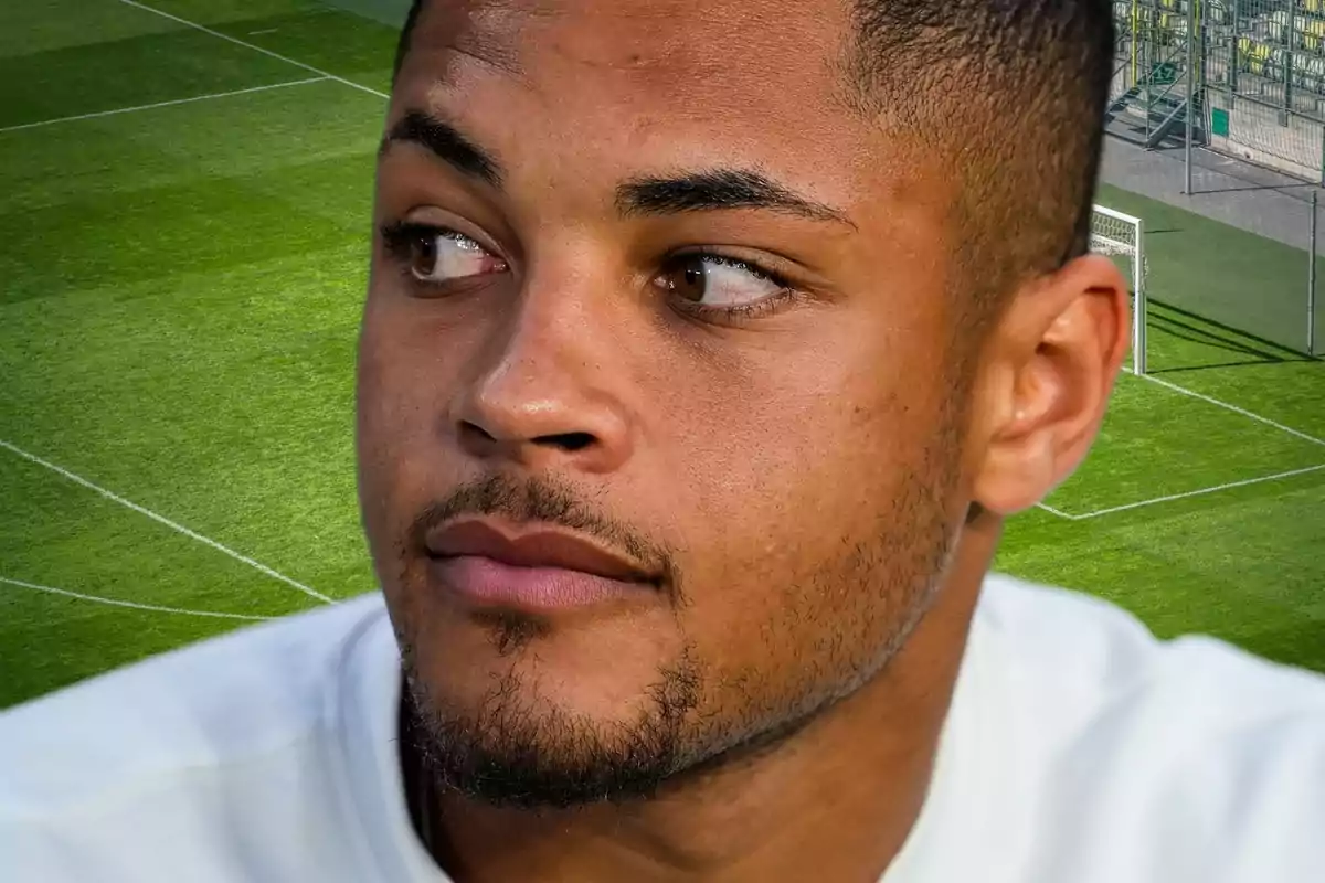 Un hombre con barba corta y cabello corto mira hacia un lado, con un campo de fútbol de fondo.