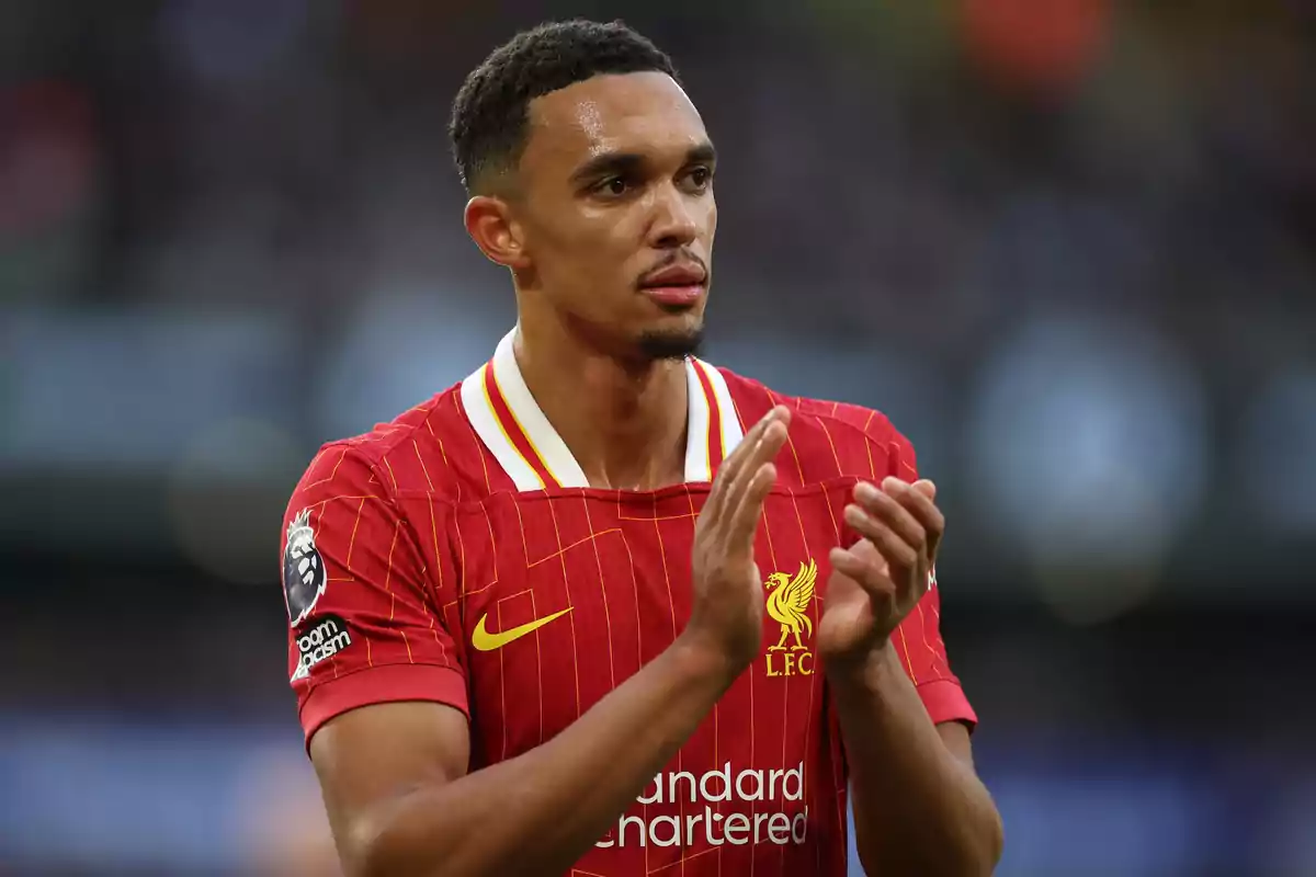 A soccer player in a red uniform applauds on the field.