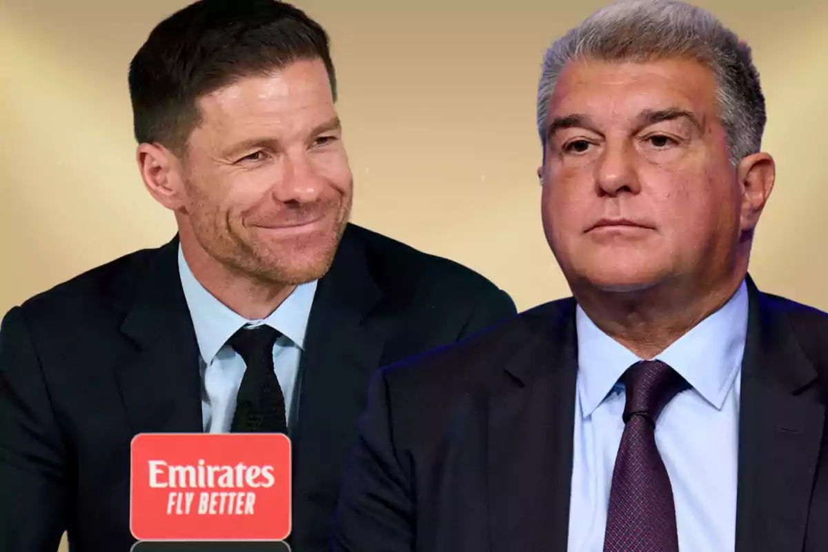 Two men in suits pose together in front of a beige background; one of them is smiling while the other has a serious expression, and in the foreground there is a microphone with the Emirates Fly Better logo.