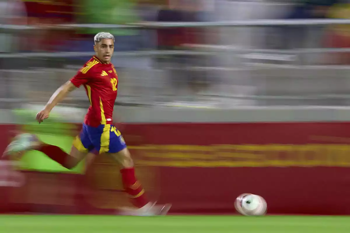 Soccer player running on the field in red and blue uniform while chasing the ball. Soccer player running on the field in red and blue uniform while chasing the ball.